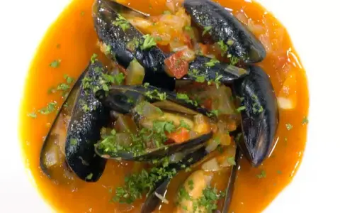 Mejillones a la marinera, jugosos y frescos, nadan en una salsa roja vibrante con perejil picado.