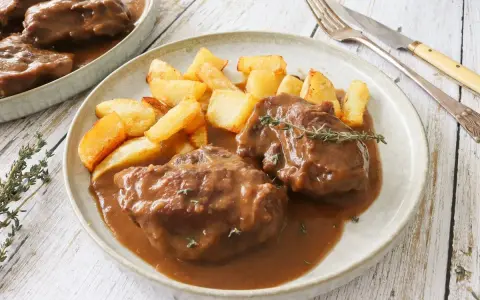 Dos tiernas porciones de pata de ternera guisada en su jugo, acompañadas de patatas rústicas fritas y una ramita de tomillo.