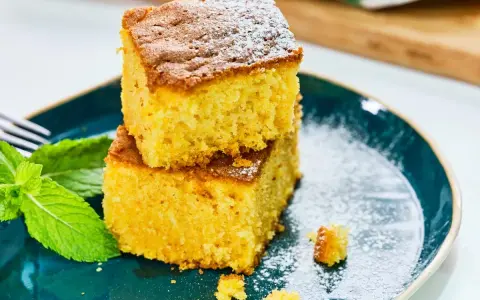 Dos porciones de bizcocho de calabaza espolvoreadas con azúcar glas, acompañadas de hojas de menta fresca en un plato azul.