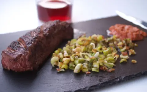Un jugoso onglet de ternera a la parrilla, acompañado de verduras salteadas y una guarnición rojiza.