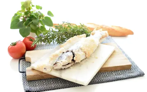 Lubina a la sal lista para servir, acompañada de tomates frescos, romero y pan rústico.