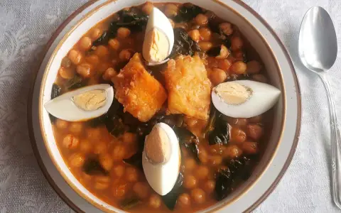 Un reconfortante potaje de vigilia con garbanzos, espinacas, trozos de bacalao rebozado y huevos cocidos, listo para disfrutar.