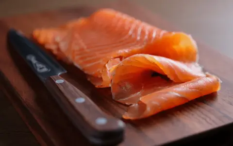 Finísimas lonchas de salmón marinado, listas para disfrutar, junto a un cuchillo de chef sobre tabla de madera.