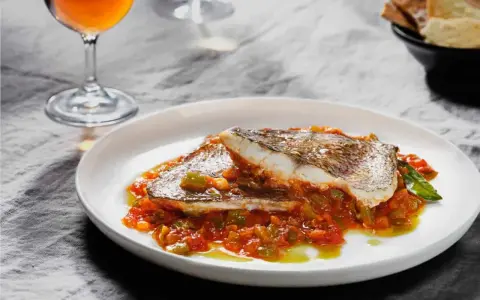 Deliciosa urta a la roteña servida en plato blanco, con vino y pan tostado al fondo.