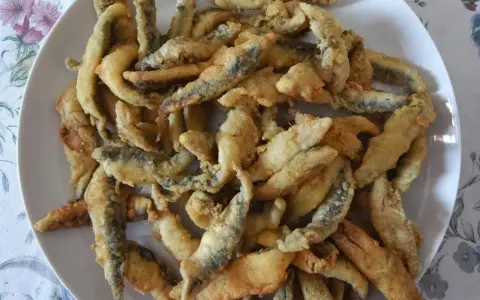 Un plato blanco lleno de boquerones fritos crujientes, listos para disfrutar.