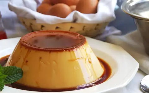 Delicioso flan de huevo casero con caramelo líquido, decorado con menta. En el fondo, una cesta con huevos frescos.