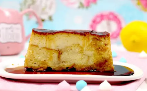 Un trozo de pan de calatrava con caramelo líquido, sobre un plato blanco, con merengues de colores y un limón al fondo.