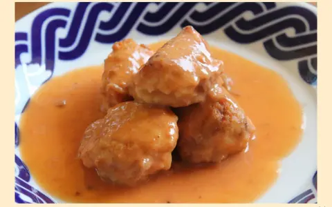 Deliciosas albóndigas de rape en una cremosa salsa naranja, servidas en un plato con borde azul.