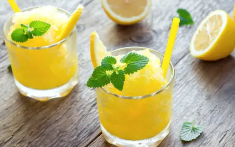 Refrescante granizado de limón, perfecto para un día caluroso. Servido en vasos con rodajas de limón y hojas de menta.