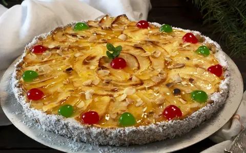 Deliciosa tarta de manzana cubierta de almendras laminadas y cerezas rojas y verdes. El borde está cubierto de coco rallado.