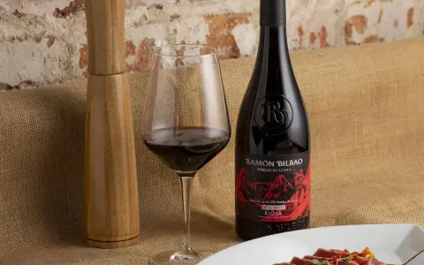 Una copa de vino seco, una botella de Ramón Bilbao Rioja y un plato de atún sellado, listos para una cena.