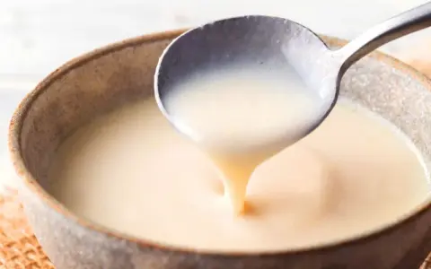 Cuchara sirviendo crema inglesa cremosa en un cuenco rústico.