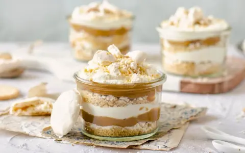 Postres en vaso con capas de bizcocho, crema y dulce de leche, coronados con merengue y polvito canario.