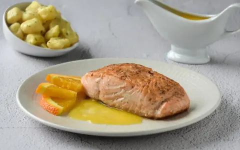 Filete de salmón a la naranja, servido con gajos de naranja y una salsa dorada. Acompañado de gnocchis en un cuenco.
