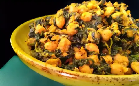 Un plato amarillo lleno de garbanzos con espinacas, un guiso saludable y sabroso.