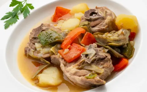 Cordero guisado receta tradicional con patatas, zanahorias y alcachofas en un plato blanco.