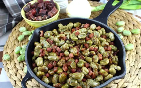 Habas tiernas salteadas con trocitos de jamón en una sartén de hierro fundido, un plato tradicional y delicioso.
