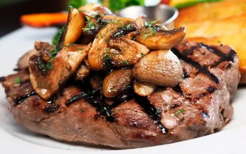 Solomillo de ternera guisado con champiñones salteados y perejil picado, servido en un plato blanco.
