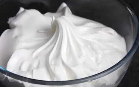 Merengue italiano esponjoso y brillante en un bol de cristal, listo para decorar postres.