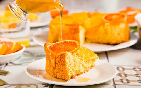 Un trozo de tarta de naranja esponjosa, decorado con una rodaja de naranja y bañado en un almíbar dorado.