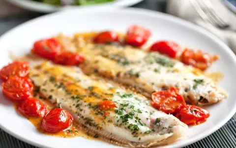 Dos filetes de lenguado a la plancha, servidos con tomates cherry salteados y perejil picado.