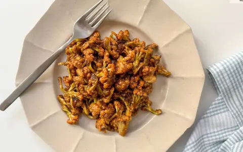 Coliflor glaseada, una de las mejores recetas con coliflor. Servida en plato beige con tenedor plateado y servilleta a cuadros.