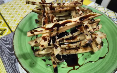 Berenjenas fritas en forma de bastones, bañadas en miel oscura, servidas en un plato verde.
