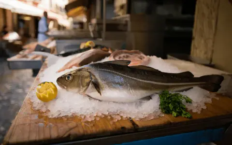 Pescado fresco en hielo, listo para deliciosas recetas de bacalao. Limón y perejil acompañan.