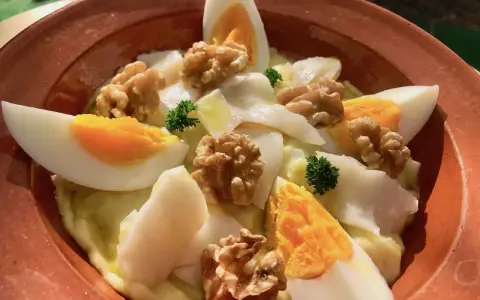 Delicioso plato de atascaburras receta con huevo duro, nueces y perejil en una cazuela de barro.