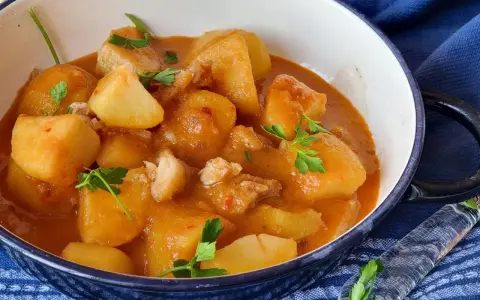 Un reconfortante plato de patatas con bacalao en una salsa rojiza, adornado con perejil fresco.