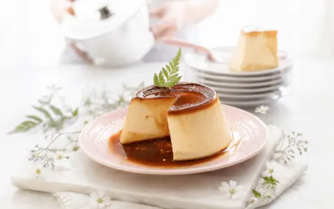 Delicioso flan de queso con caramelo líquido, decorado con una ramita verde. Se apilan más porciones en el fondo.