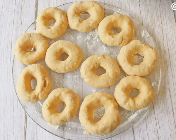 Un plato transparente muestra rosquillas caseras esponjosas, listas para hornear.
