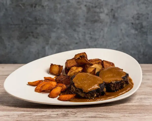 Delicioso plato de cola de toro en salsa, acompañado de patatas rústicas y zanahorias glaseadas.