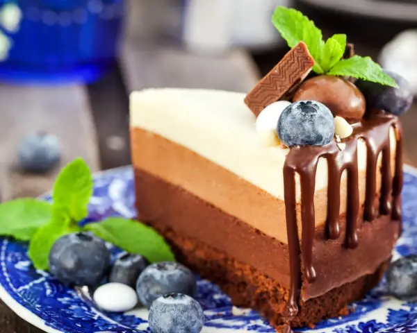 Deliciosa tarta de tres chocolates, con capas de chocolate blanco, con leche y negro, decorada con arándanos y menta.
