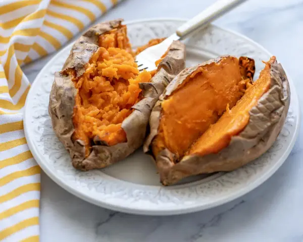 Dos mitades de boniato asado en freidora de aire, servidas en un plato blanco con un tenedor.