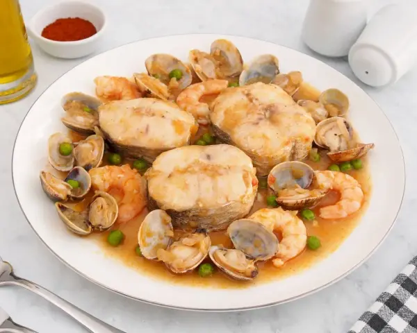 Merluza a la cazuela con gambas, almejas y guisantes en una salsa sabrosa.