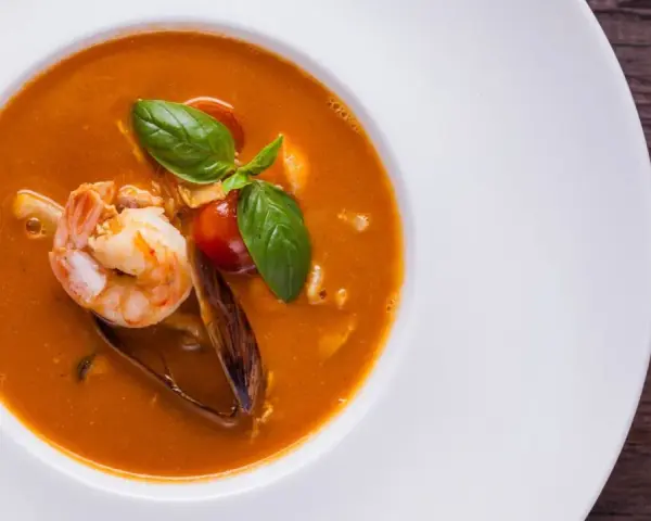 Un plato de zarzuela de pescado con gambas, mejillones y tomate, decorado con albahaca fresca.
