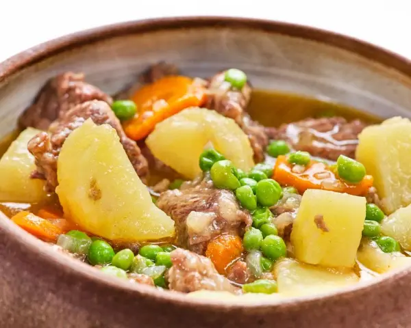 Un reconfortante ragú con trozos de carne tierna, patatas, zanahorias y guisantes en un cuenco rústico.
