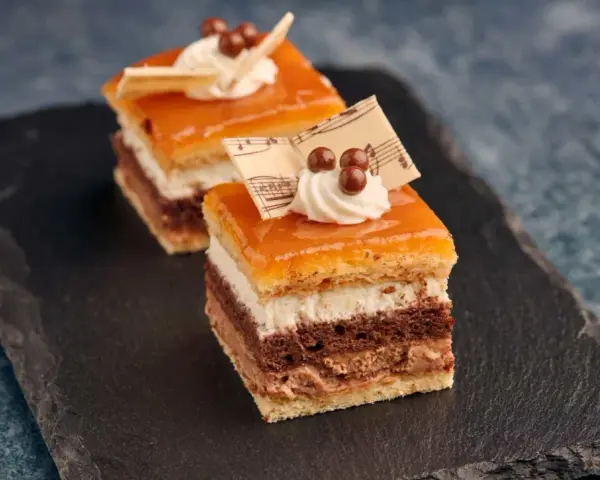 Deliciosa tarta San Marcos en porciones, con capas de bizcocho, crema y cobertura anaranjada, decorada con nata y notas musicales de chocolate.