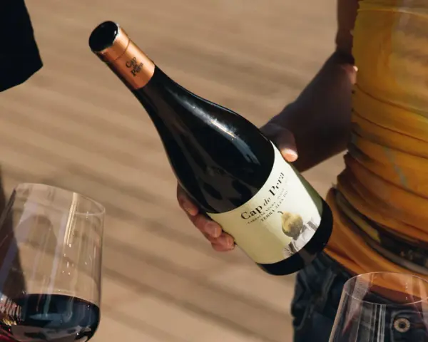 Manos sirven vino tinto de una botella Cap de Pera. Opiniones sobre "llàgrimes de tardor" y la experiencia.