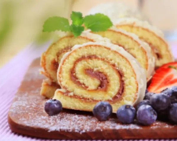 Brazo de gitano en rodajas con fresas y arándanos sobre tabla de madera.