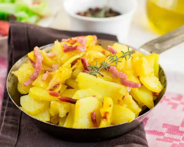 Patatas al microondas con trocitos de bacon crujiente y romero fresco, servidas en una sartén metálica. ¡Un plato sencillo y delicioso!