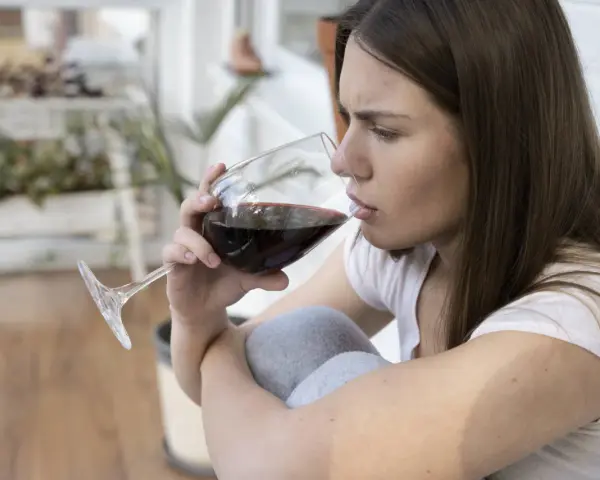 Mujer pensativa bebe vino tinto, recordando que el vino engorda.