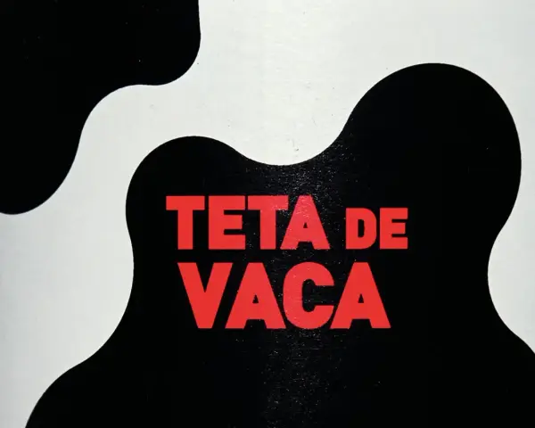 Texto rojo "TETA DE VACA" sobre un fondo blanco y negro con manchas de vaca.