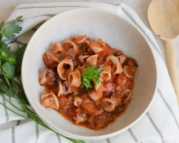 Deliciosos chipirones en salsa de tomate, servidos en un cuenco de cerámica, decorados con perejil fresco.