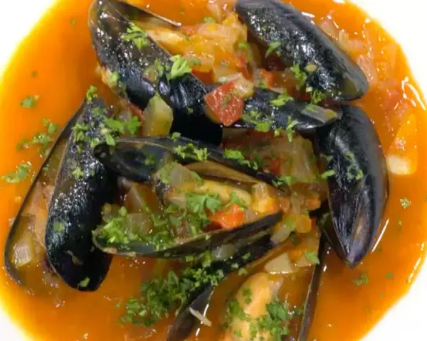 Mejillones a la marinera, jugosos y frescos, nadan en una salsa roja vibrante con perejil picado.