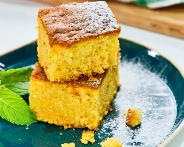 Dos porciones de bizcocho de calabaza espolvoreadas con azúcar glas, acompañadas de hojas de menta fresca en un plato azul.