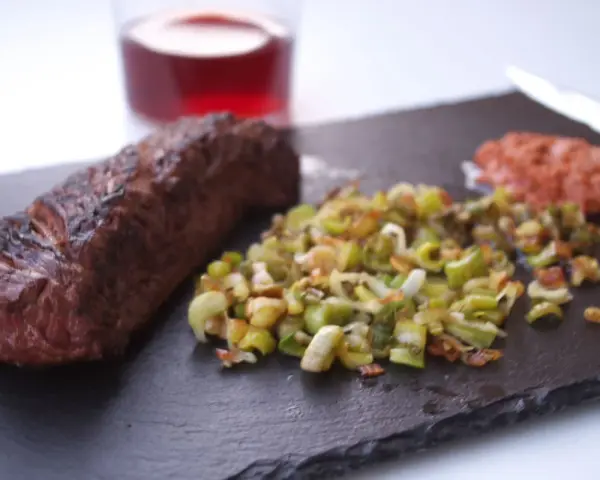 Un jugoso onglet de ternera a la parrilla, acompañado de verduras salteadas y una guarnición rojiza.
