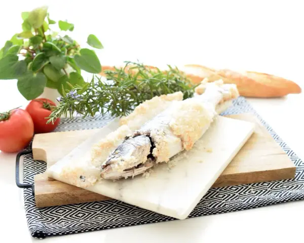 Lubina a la sal lista para servir, acompañada de tomates frescos, romero y pan rústico.