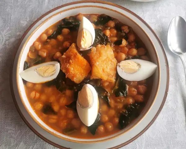 Un reconfortante potaje de vigilia con garbanzos, espinacas, trozos de bacalao rebozado y huevos cocidos, listo para disfrutar.